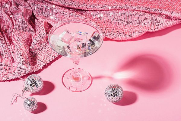 Cocktail drink served on a pink table with a pink glittery cloth and small silver balls next to it