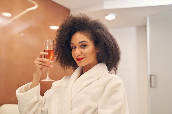 A woman in a white robe raising a glass of bubbles
