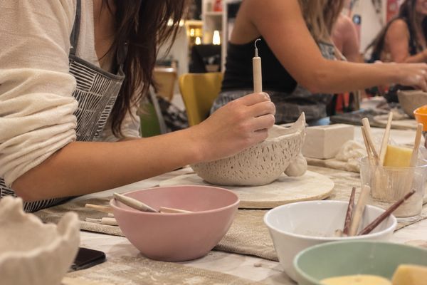 Hands shaping a textured clay bowl beside pastel mixing bowls and tools