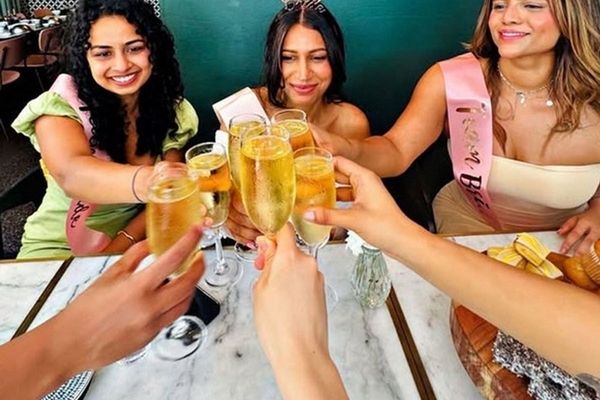 Friends in sashes clinking glasses of bubbly across the table