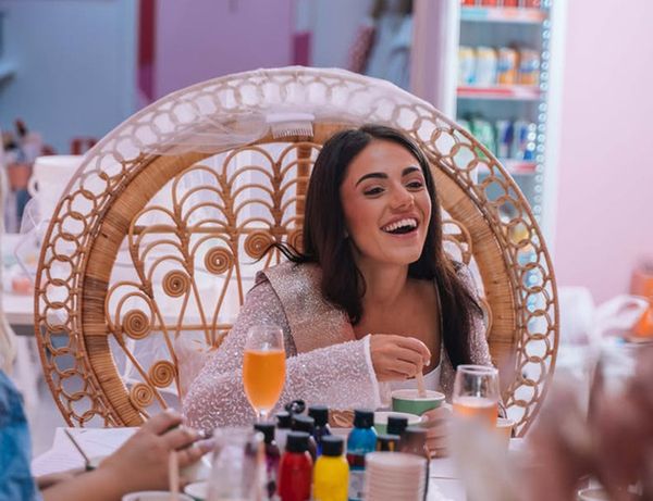 A guest laughing in a peacock chair at a studio table set with spritz cocktails and colours