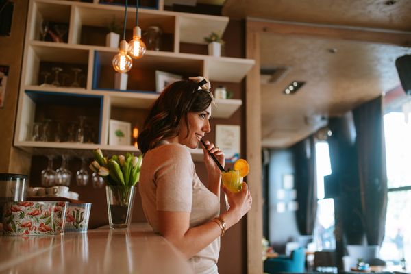 A woman singing into a microphone with a cocktail in a sunny bar