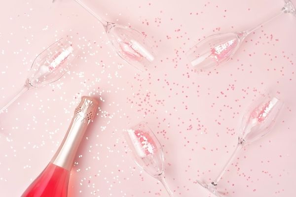 Champagne flutes and a bottle of rose among pink heart confetti