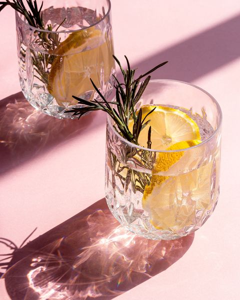 Two gin cocktails with lemon and rosemary on a pink table