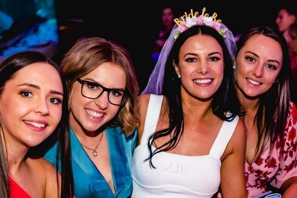 Smiling bride in a white top and veil headband with three friends at night