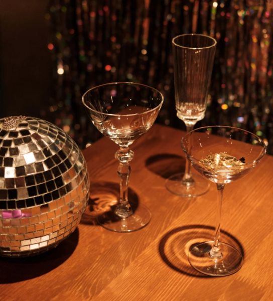 A mirror disco ball beside cocktail glasses on a wooden table