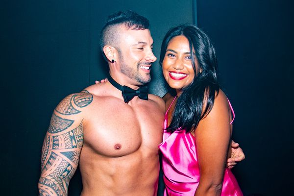 Shirtless waiter in a bow tie with his arm around a smiling woman in pink satin