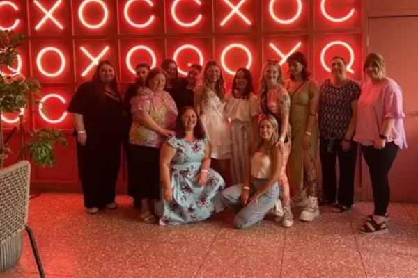 Hens group posing together in front of a wall of glowing red neon letters