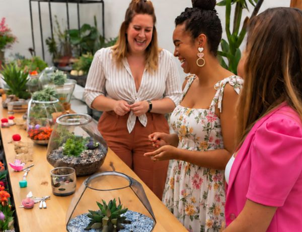 Friends laughing together beside a long table of glass terrariums