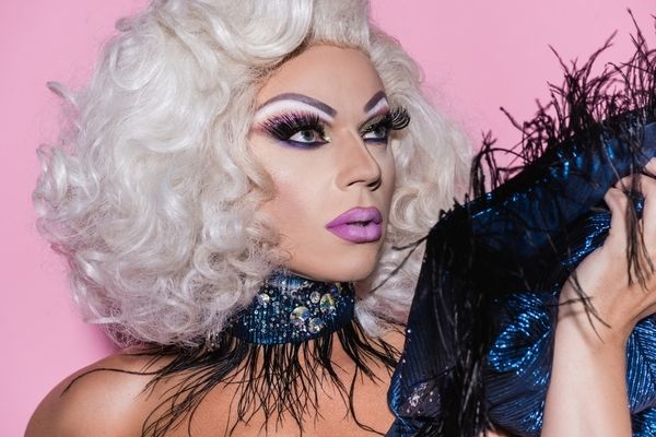 A drag queen in a platinum wig and feather collar looking over her shoulder