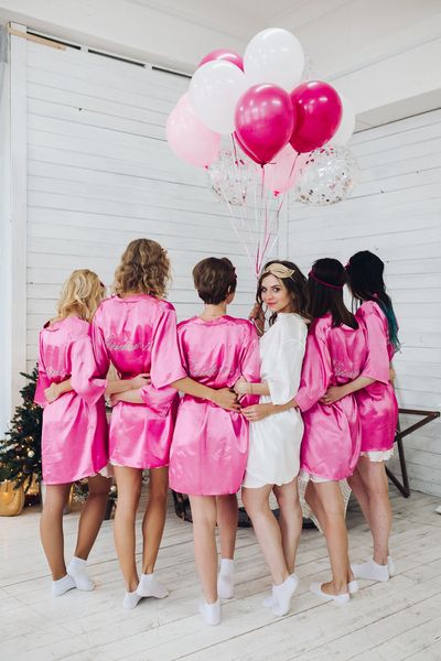 A hens group in pink robes with the bride to be in white beneath pink balloons