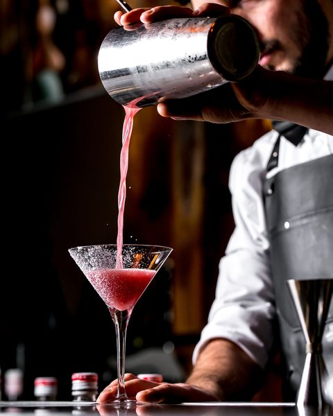 A mixologist is pouring a cocktail drink from a shaker into a glass during the cocktail making class