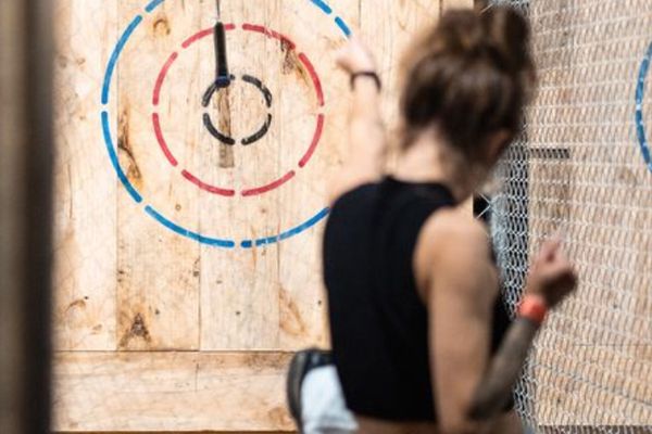Woman throws an axe at a wooden target with a blade stuck near the bullseye