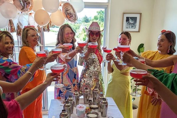 The bride in a Bride cowboy hat and her friends raising pink cocktails over the class table