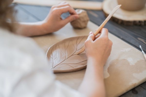 Hen meticulously polishes her leaf-shaped plate with a brush at the clay pottery workshop
