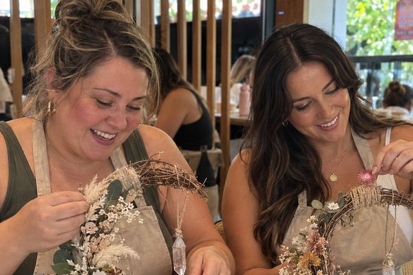 Two friends in aprons add dried flowers and crystals to crescent moon wreaths