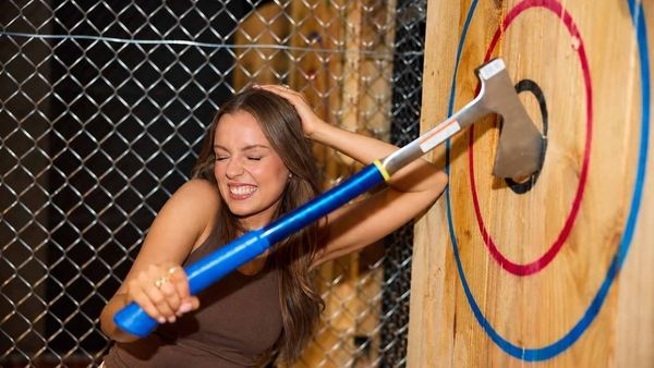 A hen laughing as she lands an axe in the centre of a wooden target