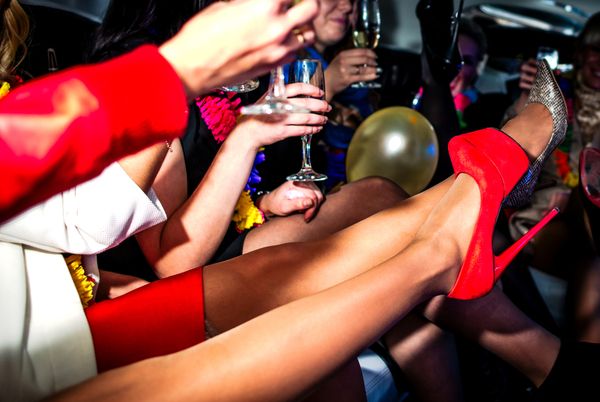 Friends in heels and party dresses kicking up their legs inside a limousine