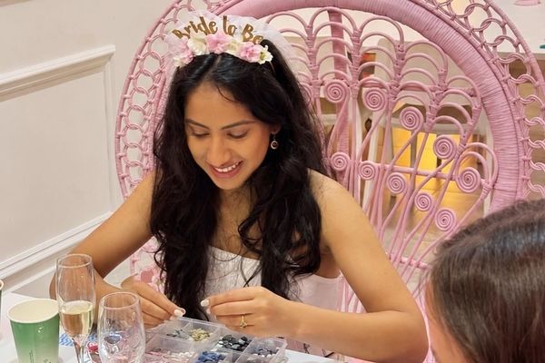 A smiling bride to be in a floral headband picking glass tiles for her mosaic in a pink peacock chair