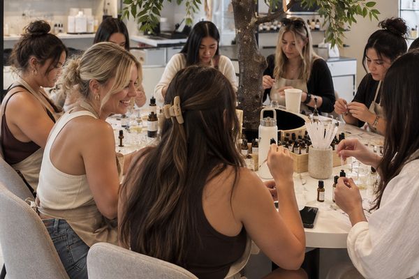 A big group of friends blending perfume together at round tables under a leafy indoor tree