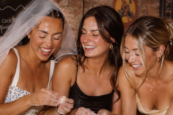 A bride in a veil laughing with two friends as they roll gnocchi by hand