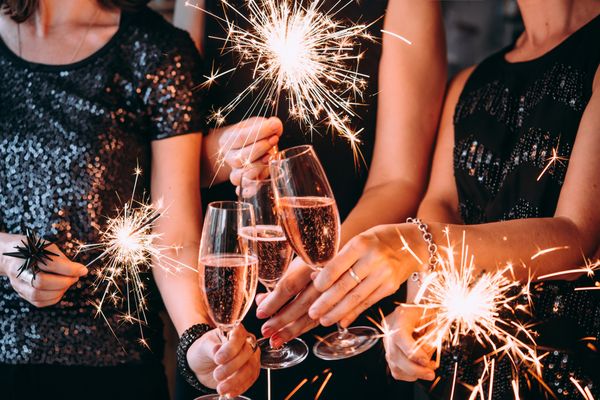 Friends in sequins raising pink bubbles and sparklers together