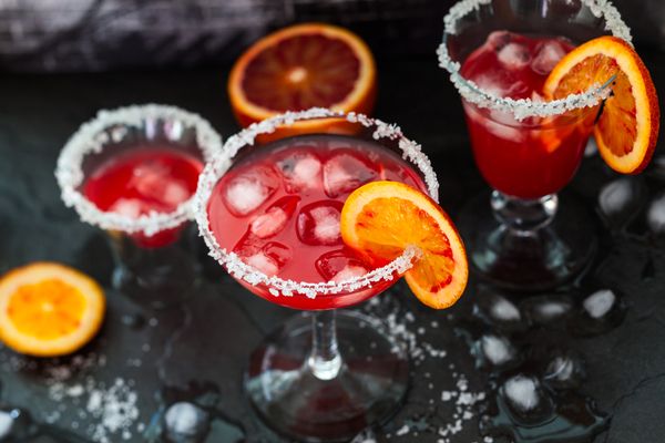 Red cocktails with salted rims and blood orange slices on a dark table