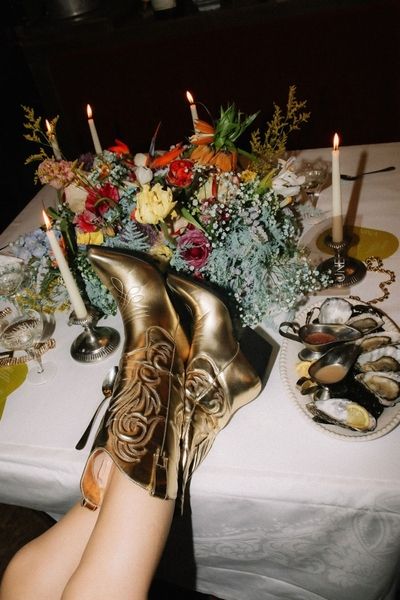 Gold cowboy boots up on a dinner table set with flowers and candles