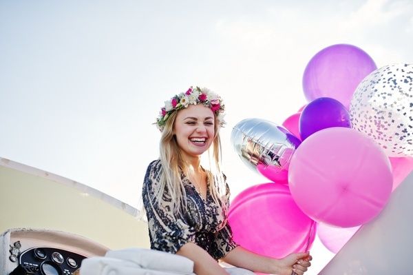 A gorgeous hen dressed in a blue outfit and a flower crown smiles, and holds colourful balloons on her private boat cruise