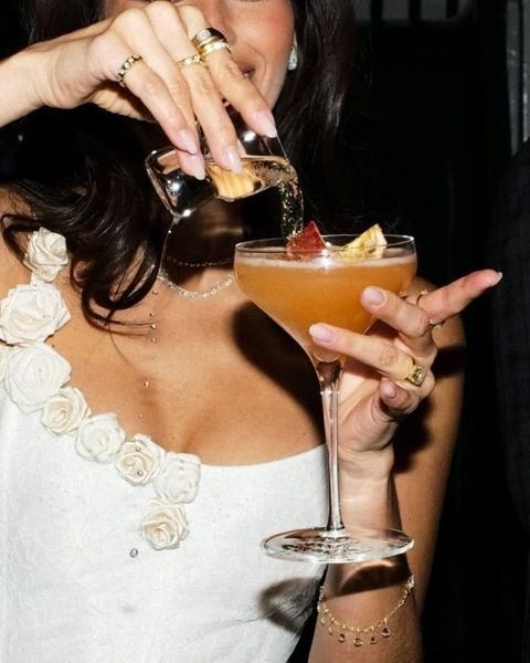 A woman pouring a cocktail into a coupe glass