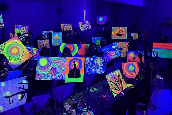 A hens crew holding up their canvases glowing bright under UV light