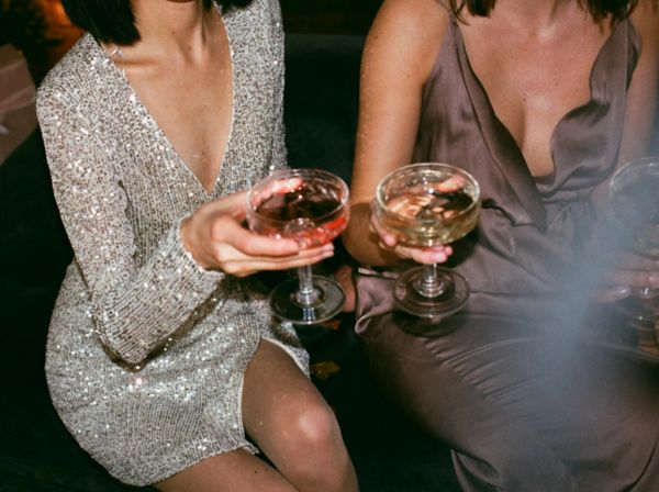 Two friends in sequin dresses holding pink cocktails in coupes