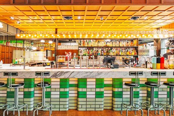 A green and white tiled bar with stools under warm golden ceiling lights