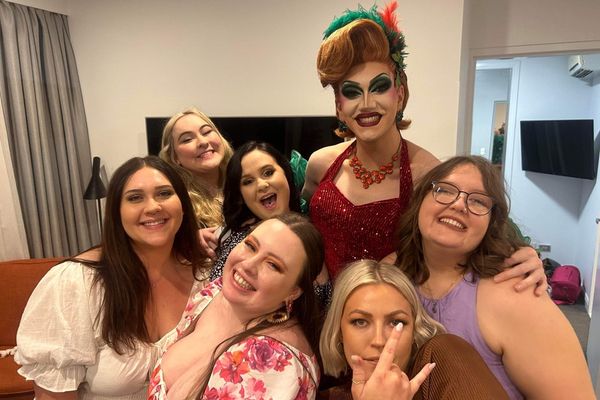 Drag queen in red sequins poses with a laughing group of hens indoors