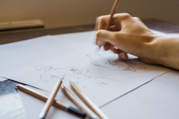 Pencils and canvas being drawn on by a delicate hand