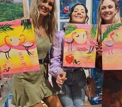 Three friends holding up their flamingo paintings