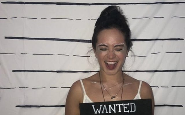 A laughing woman holding a Wanted sign in front of a height chart