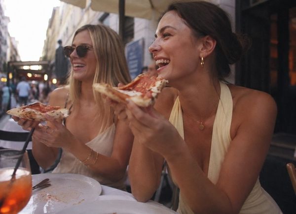 Two friends laughing as they bite into slices of pizza