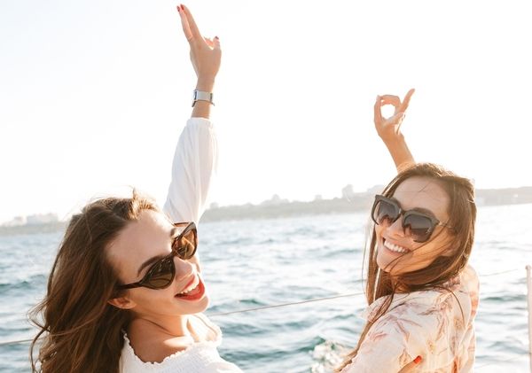 Two friends in sunglasses laughing with their arms up on a boat