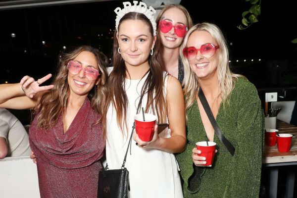 Bride in a crown with friends in heart sunglasses smiling on a waterfront deck