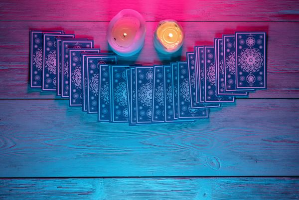 A deck of tarot cards spread out beside two candles on a blue table