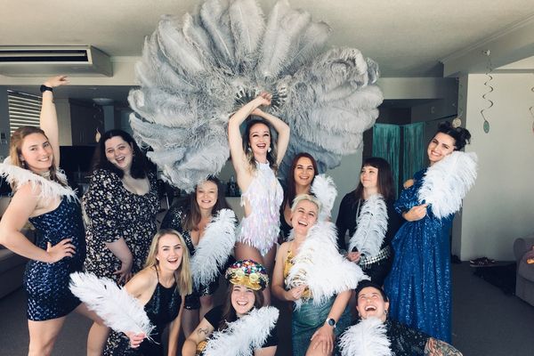 Hens group posing with white and grey feather fans at a burlesque class