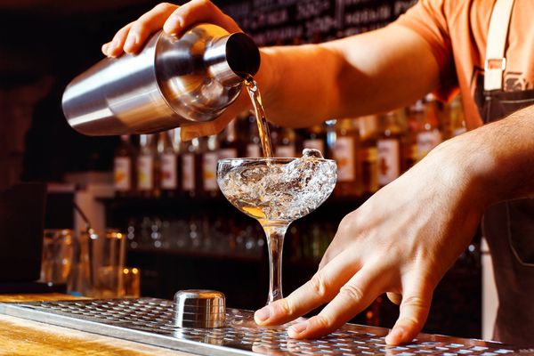A bartender pouring a cocktail from a shaker into a coupe glass