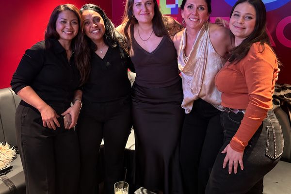 Five women standing together at a VIP booth table under red and purple lights