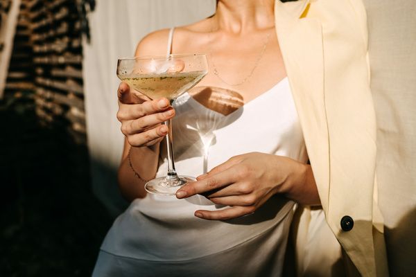 Lovely hen wearing an elegant dress with a champagne glass in her hand and leaning against the white wall