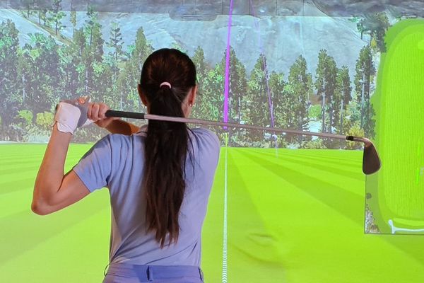 Woman lines up a shot in front of a bright green golf simulator fairway