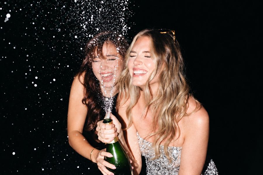 Two friends laughing as a champagne bottle sprays