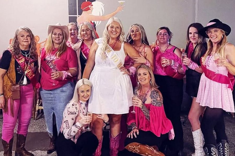 A cowgirl hens group in pink, hats and boots, around the bride in white