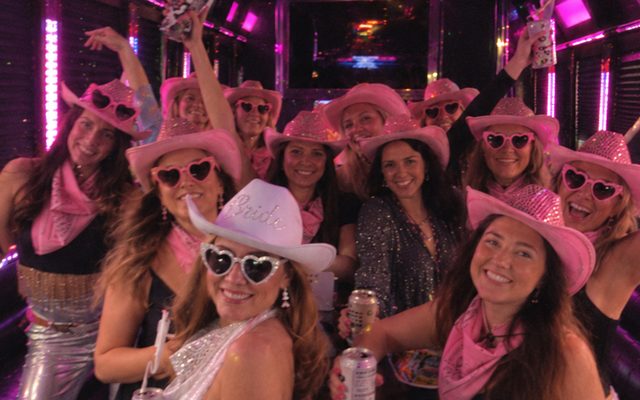 A hens group in pink cowgirl hats and heart sunglasses on a party bus