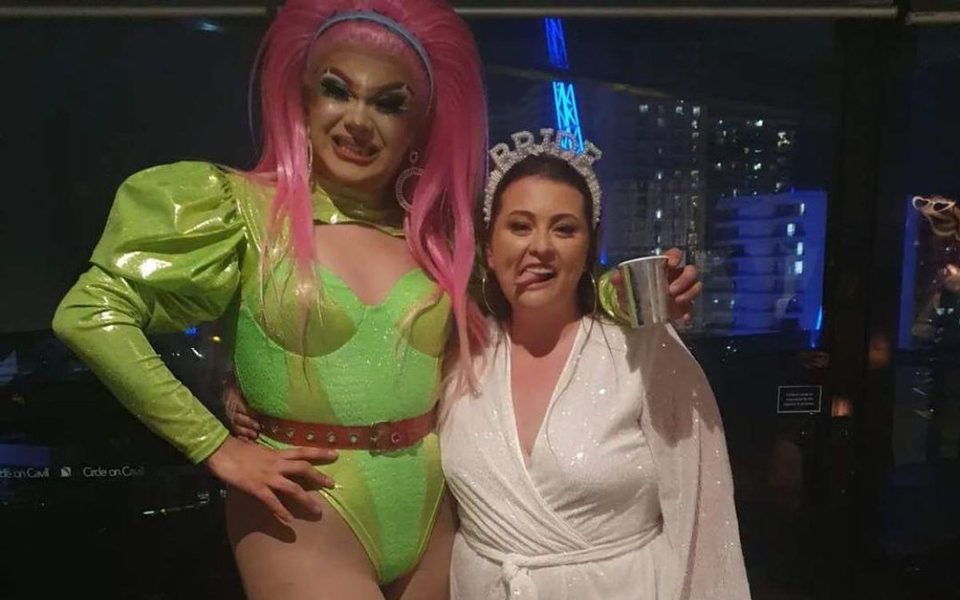 A drag queen in lime green and pink hair posing with the bride to be in white